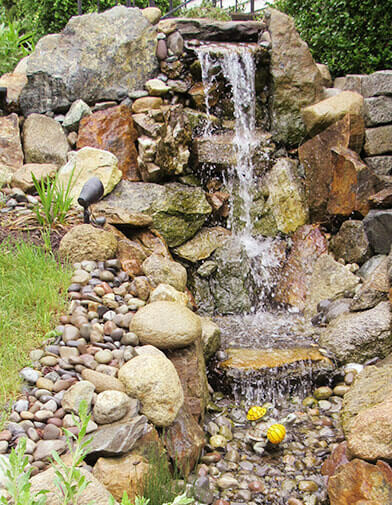 a beautiful stone water fountain flows into a mini stream surrounded by river rock