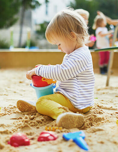 two-year-old child plays with small pails in the sandbox