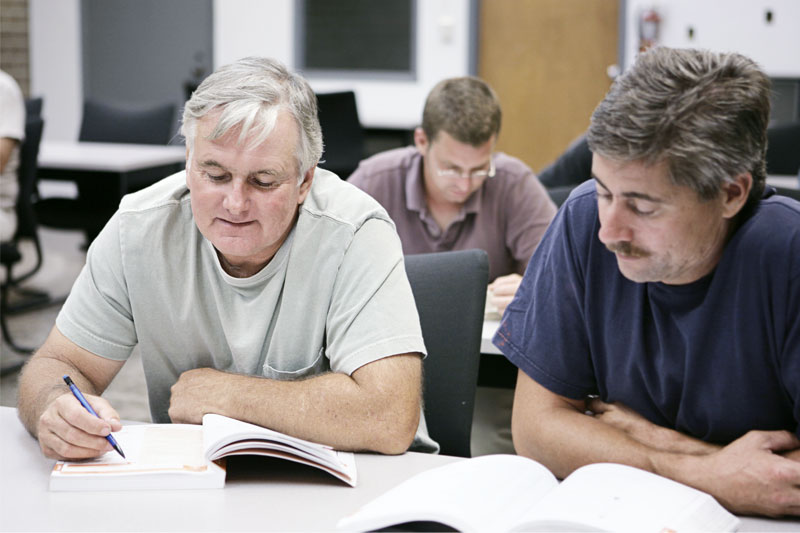 Two middle-aged men referring to a book in a training session